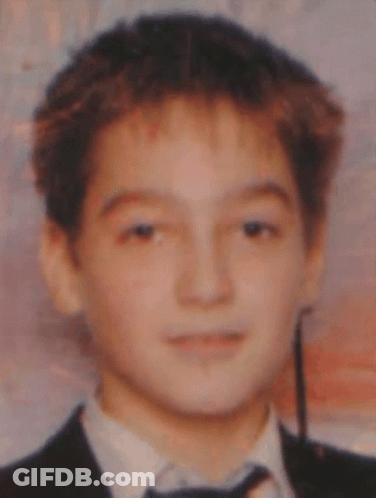 A Young Boy Wearing A Suit And Tie Looks At The Camera GIF