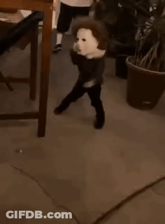 A Young Boy Wearing A White Mask Is Standing Next To A Potted Plant . GIF