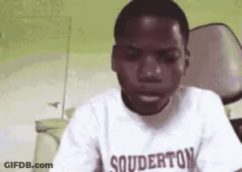 A Young Boy Wearing A White T-Shirt With The Word Souderton On It Is Sitting In A Chair . GIF