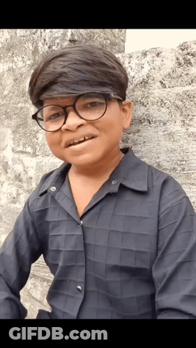 A Young Boy Wearing Glasses And A Black Shirt Is Smiling For The Camera GIF