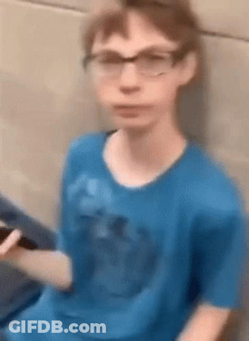 A Young Boy Wearing Glasses And A Blue Shirt Is Sitting On A Couch Holding A Cell Phone . GIF