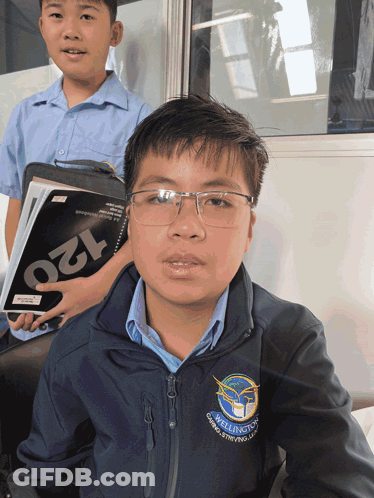 A Young Boy Wearing Glasses And A Jacket That Says Wellington On It GIF