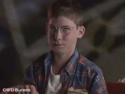 A Young Boy Wearing Glasses And A Plaid Shirt Is Sitting In A Chair And Making A Funny Face . GIF