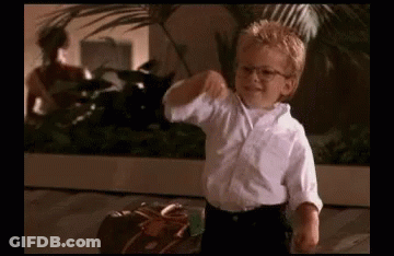 A Young Boy Wearing Glasses And A White Shirt Is Standing Next To A Suitcase And Giving A Thumbs Up . GIF