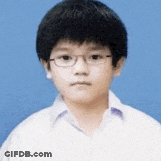 A Young Boy Wearing Glasses And A White Shirt Looks At The Camera . GIF