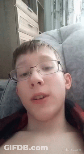 A Young Boy Wearing Glasses Is Laying On A Bed Without A Shirt . GIF