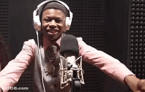 A Young Boy Wearing Headphones And A Pink Shirt Is Standing In Front Of A Microphone GIF