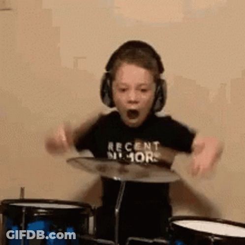 A Young Boy Wearing Headphones Is Playing Drums And Making A Funny Face . GIF