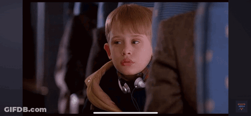 A Young Boy Wearing Headphones Is Sitting On A Plane And Looking At The Camera . GIF