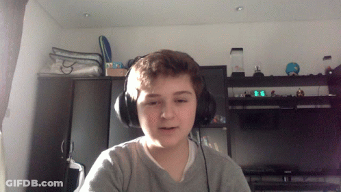 A Young Boy Wearing Headphones Looks At The Camera In Front Of A Digital Clock That Reads 9:06 GIF