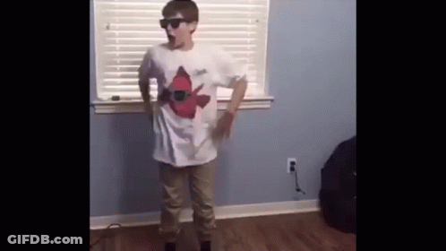 A Young Boy Wearing Sunglasses And A White Shirt Is Standing In Front Of A Window In A Room . GIF