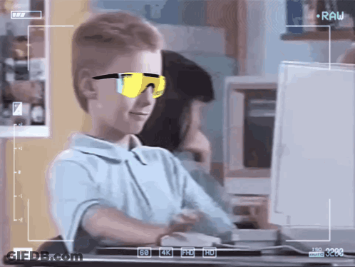 A Young Boy Wearing Sunglasses Is Sitting In Front Of A Computer Monitor GIF