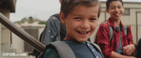 A Young Boy With A Backpack Is Smiling For The Camera While Sitting On The Stairs . GIF
