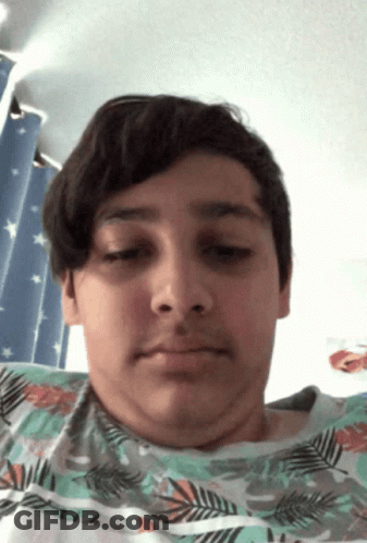 A Young Boy With A Floral Shirt On Looks At The Camera With His Eyes Closed GIF