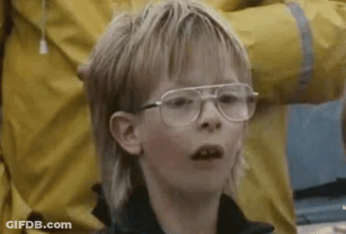 A Young Boy With A Mullet And Glasses Is Looking At The Camera . GIF