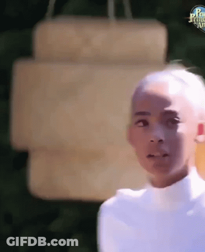 A Young Boy With A Shaved Head Is Standing In Front Of A Sign . GIF