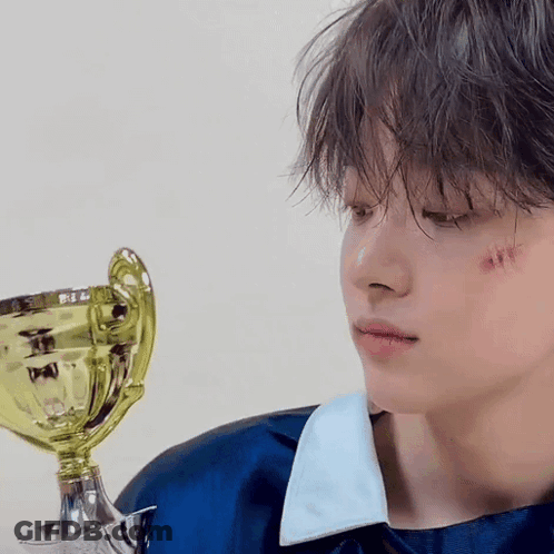 A Young Boy With A Trophy In His Hand Has A Scratch On His Face . GIF