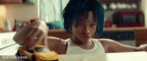 A Young Boy With Blue Hair Is Playing With A Toy Car On A Kitchen Counter . GIF