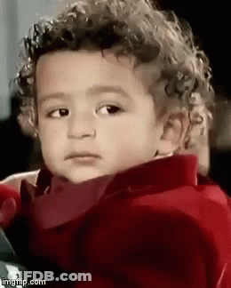 A Young Boy With Curly Hair Is Wearing A Red Jacket And Making A Funny Face . GIF