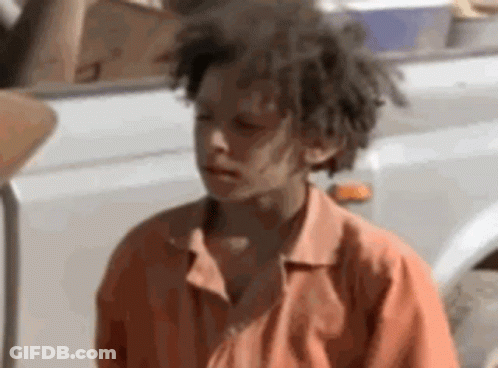 A Young Boy With Dreadlocks Is Standing Next To A White Truck . GIF