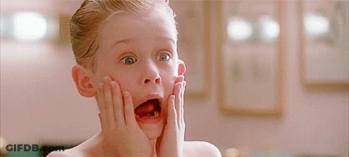 A Young Boy With His Mouth Open And His Hands On His Face Looks Surprised GIF