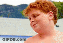 A Young Boy With Red Hair Is Standing In Front Of A Body Of Water GIF