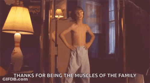 A Young Boy Without A Shirt Is Standing In A Room With His Hands On His Hips And A Lamp . GIF