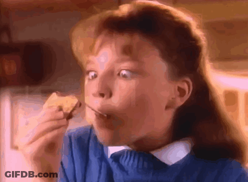 A Young Girl In A Blue Sweater Is Eating A Piece Of Food GIF