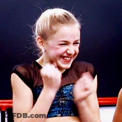 A Young Girl In A Blue Top Is Smiling And Clapping Her Hands GIF