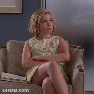 A Young Girl In A Floral Dress Sits In A Chair With Her Eyes Closed GIF