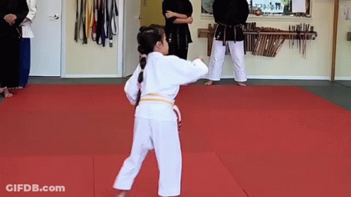 A Young Girl In A White Karate Uniform Is Standing On A Red Mat In A Gym . GIF