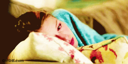 A Young Girl Is Laying On A Bed With A Blue Blanket On Her Head . GIF