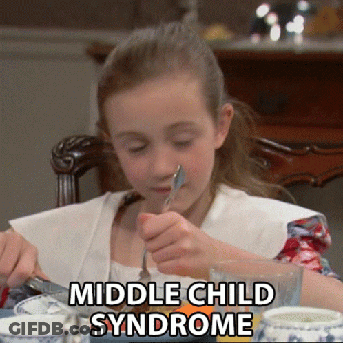 A Young Girl Is Sitting At A Table With A Fork In Her Mouth And The Words Middle Child Syndrome Written Above Her GIF