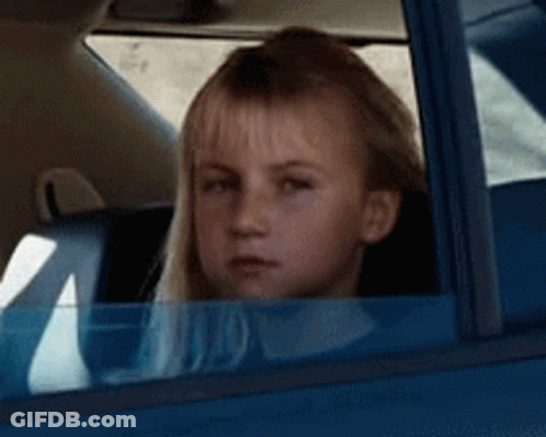 A Young Girl Is Sitting In A Blue Car Looking Out The Window . GIF