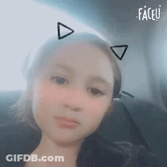 A Young Girl Is Sitting In A Car Wearing Cat Ears . GIF
