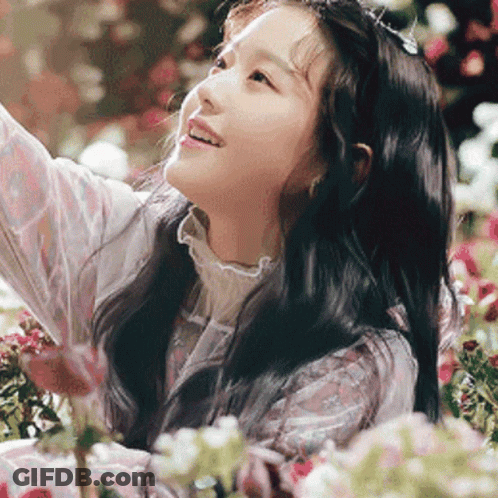 A Young Girl Is Standing In A Field Of Flowers Looking Up At The Sky . GIF