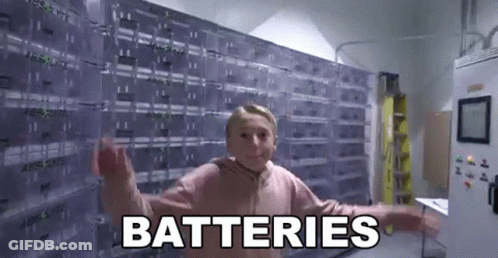 A Young Girl Is Standing In Front Of A Wall Of Batteries And Saying `` Batteries '' . GIF