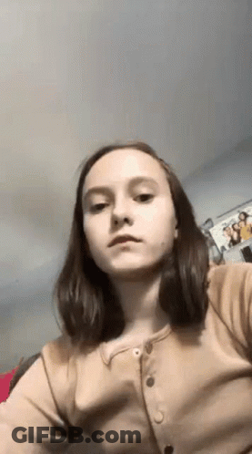 A Young Girl Is Taking A Selfie In A Room With A Picture On The Wall . GIF