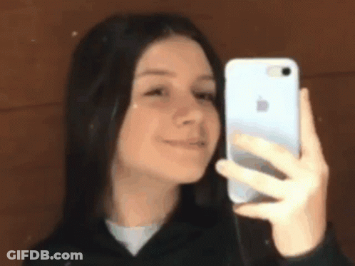A Young Girl Is Taking A Selfie With Her Phone In Front Of A Mirror . GIF