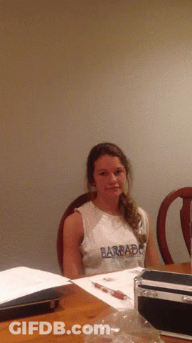 A Young Girl Wearing A Barbado Shirt Sits At A Table GIF