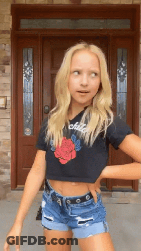 A Young Girl Wearing A Black Crop Top And Shorts Is Standing In Front Of A Door . GIF