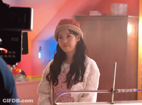 A Young Girl Wearing A Knitted Hat And A White Sweater Is Standing In Front Of A Camera . GIF
