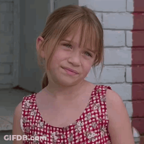 A Young Girl Wearing A Red And White Plaid Dress Stands In Front Of A Brick Wall GIF