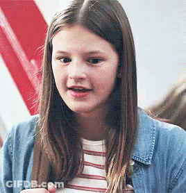 A Young Girl Wearing A Striped Shirt And A Denim Jacket Is Looking At The Camera . GIF