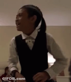 A Young Girl Wearing A Vest And A Bow Tie Is Dancing In A Room . GIF