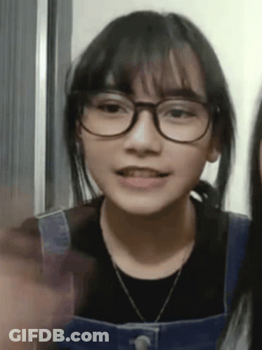 A Young Girl Wearing Glasses And Overalls Is Talking To Another Girl . GIF