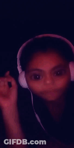 A Young Girl Wearing Headphones Is Smiling And Making A Funny Face GIF