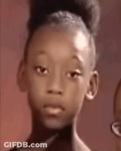 A Young Girl With A Bun On Her Head Is Looking At The Camera With A Sad Look On Her Face . GIF