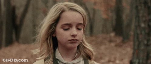 A Young Girl With Blonde Hair Is Standing In The Woods With Her Eyes Closed And Her Hair Blowing In The Wind . GIF