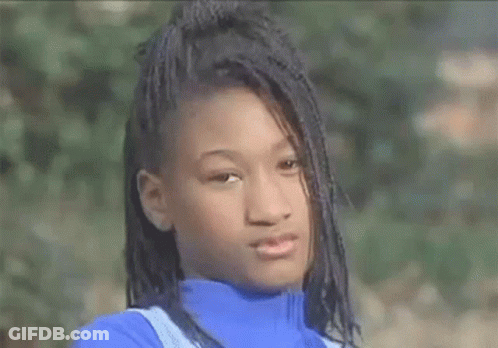 A Young Girl With Braids Is Wearing A Blue Turtleneck Sweater And Looking At The Camera . GIF